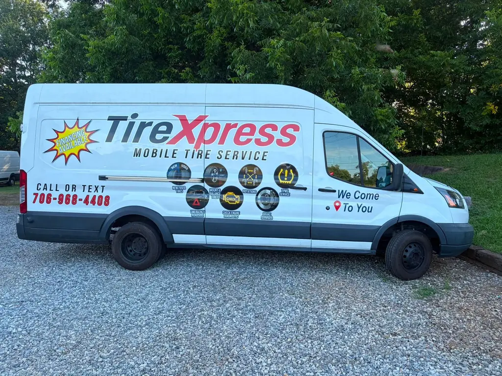 White TireXpress mobile tire service van parked on gravel, lettered “Call or text 706-968-4408 — We come to you”
